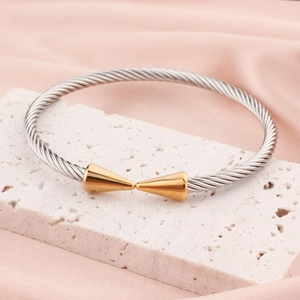 Adjustable silver cable bangle with golden cone tips on a marble and silk display