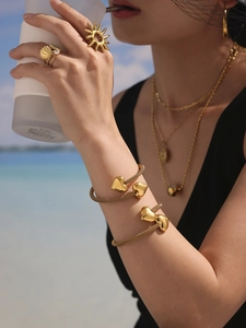 Golden hollow heart bracelets and sunburst rings styled on model in beach setting
