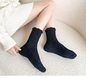 Detailed close-up of thick black coral fleece sleep socks worn on a white plush surface