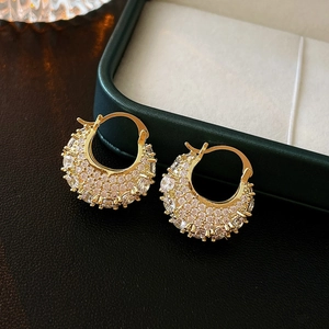 Detailed close-up of C-shaped handbag earrings with zircon inlay on premium black texture