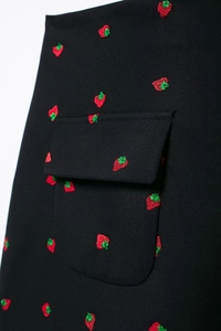 Détail d'un blazer noir avec de magnifiques broderies de fraises rouges sur la poche du vêtement