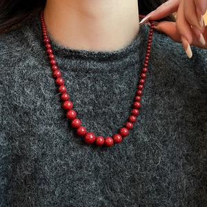 Détail d'un collier de perles rouges sur un mannequin portant un pull en maille gris