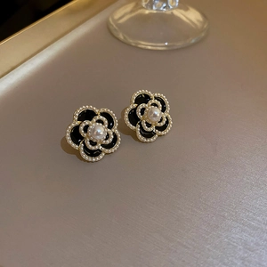 Elegant black camellia earrings with gold trim and pearls on a warm aesthetic background