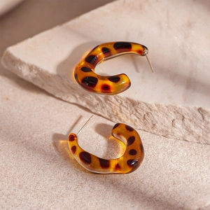 Close-up of C-shaped amber tortoise shell resin earrings on a minimalist stone texture