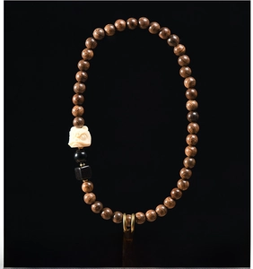 Macro detail of dark wood beads with a white carved mythical beast charm and metal ring
