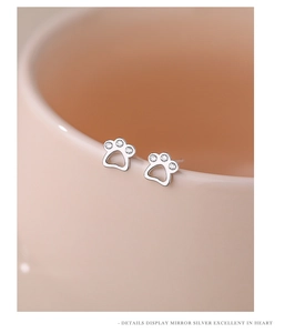 Close-up of mirror silver cat paw stud earrings with three zircons on pink ceramic