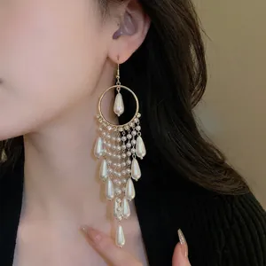 Elegant gold drop earrings with pearl tassels and crystal accents on a model
