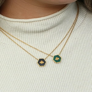 Close-up of double layer gold necklaces with hexagonal bee pendants in black and green