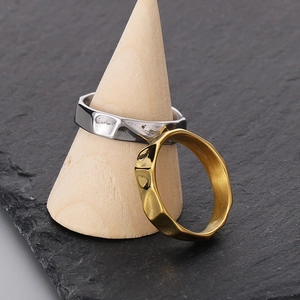 Irregular textured stainless steel rings in gold and silver finish on wooden cone