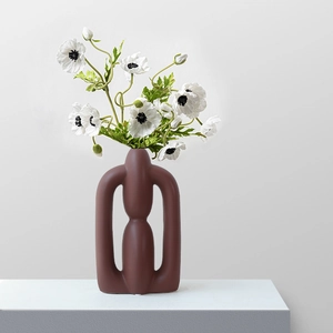 Nordic minimalist abstract hollow ceramic vase in matte reddish brown on a pedestal
