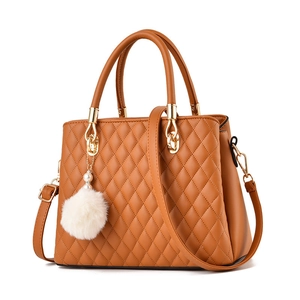 Elegant brown quilted tote bag with white pom-pom charm and removable strap in studio light