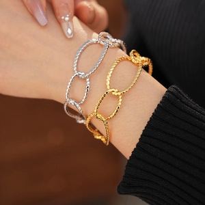 Close-up of chunky gold and silver interlocking oval link bracelets on a wrist