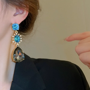 Detail of vintage earrings with blue gemstones and grey drop pearls worn by a model
