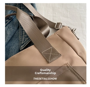 Close-up of khaki nylon tote showing X-shaped reinforced stitching and metal buckle
