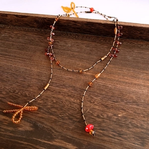 Detail of amber and red beaded necklace with bow and mushroom charms on wooden surface