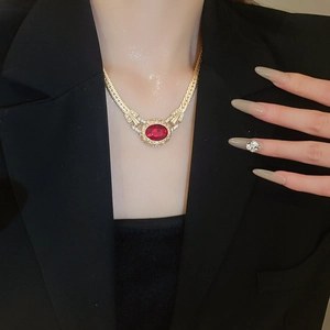 Detailed view of vintage gold necklace with oval red gemstone worn over black blazer