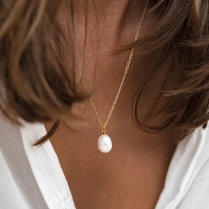 Macro shot of a minimalist gold necklace featuring a single teardrop baroque pearl pendant