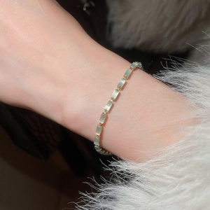 Detail of light green rectangular stone bracelet with gold links on a white fuzzy sleeve