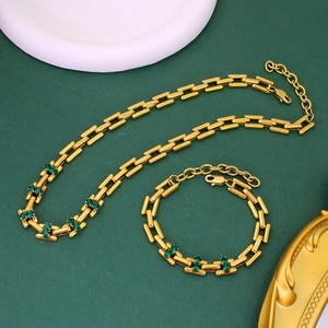 Detail of gold chain necklace and bracelet set with green gemstones on green background