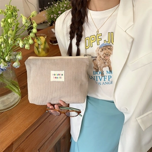 Beige corduroy cosmetic bag with bozakka beaute label held by a woman in a casual setting