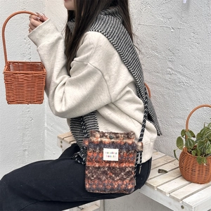 Detail of plush crossbody bag with colorful woven texture and logo label on white bench
