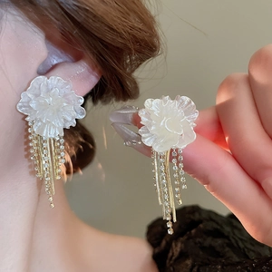 Detail of elegant white floral earrings with sparkling rhinestone tassel chains on model