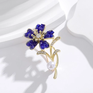 Macro detail of a gold flower brooch with blue crystal petals and a hanging white pearl