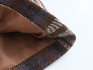 Detailed close-up of brown plaid wool coat fabric with smooth inner lining and stitching