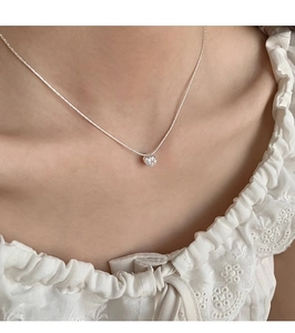Close-up of a delicate silver zircon necklace with a heart-shaped pendant on a woman