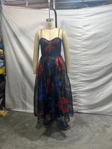 Détail d'une robe mi-longue en organza avec fleurs rouges sur un bustier noir froncé