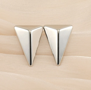 Macro shot of silver polished 3D triangle stud earrings on a beige silk background