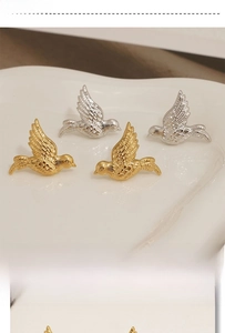 Detailed close-up of bird-shaped metallic earrings in gold and silver finish on a ceramic tray