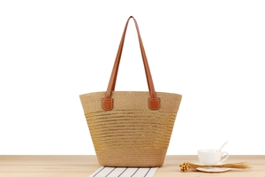 Detail of woven straw tote bag with gold stripes and brown leather handles on wooden table