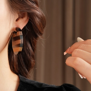 Macro side view of large geometric wooden hoop earring with striped texture worn on ear