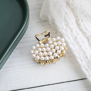 Elegant gold metal hair claw clip with white pearls in cloud shape on wood background
