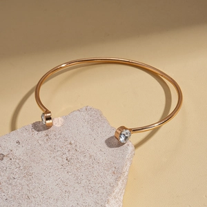 Close-up of 18k gold-plated cuff bracelet with two circular crystals on textured stone
