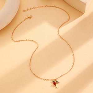 Close-up of golden hummingbird pendant with red and green gemstone accents on a thin chain