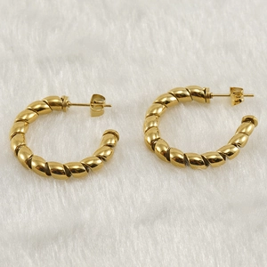 Macro detail of twisted gold-plated hoop earrings on a soft faux fur background
