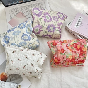 Detail of four floral makeup bags with brand label on a cozy white fabric background