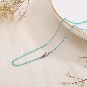 Detail of silver chain with turquoise square beads and lobster clasp on beige fabric