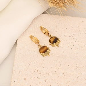 Detail view of gold stainless steel tiger eye stone drop earrings on textured stone base
