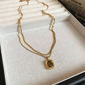 Detail of gold double-layered necklace featuring a polished snake chain and tiger eye pendant
