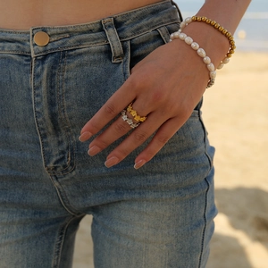 Gold and silver C-shaped flower rings with pearl and bead bracelets on a beach background