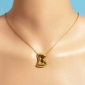 Detail of 18k gold plated letter B bubble necklace with an inlaid green heart gemstone
