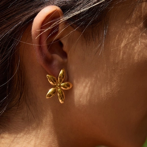 Close-up of a gold flower stud earring on a model ear with natural sunlight shadows