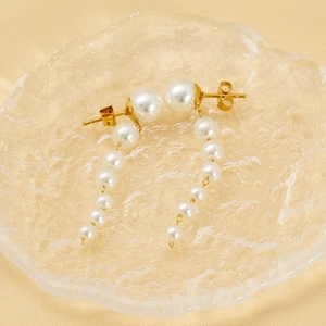 Elegant gold pearl tassel earrings with cascading white pearls on a glass display