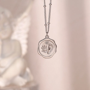 Détail du pendentif argenté avec empreintes de bébé, gravure soleil et petite pierre précieuse