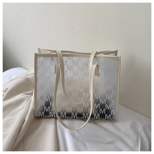 Detail of transparent tote bag with cream trim and M-letter print on white bedding