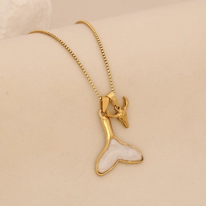 Macro detail of a golden fishtail pendant with white inlay and ox head charm on a box chain