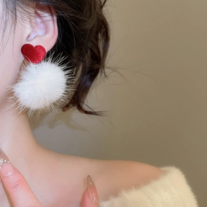 Détail d'une boucle d'oreille cœur en velours rouge avec pompon blanc sur un mannequin